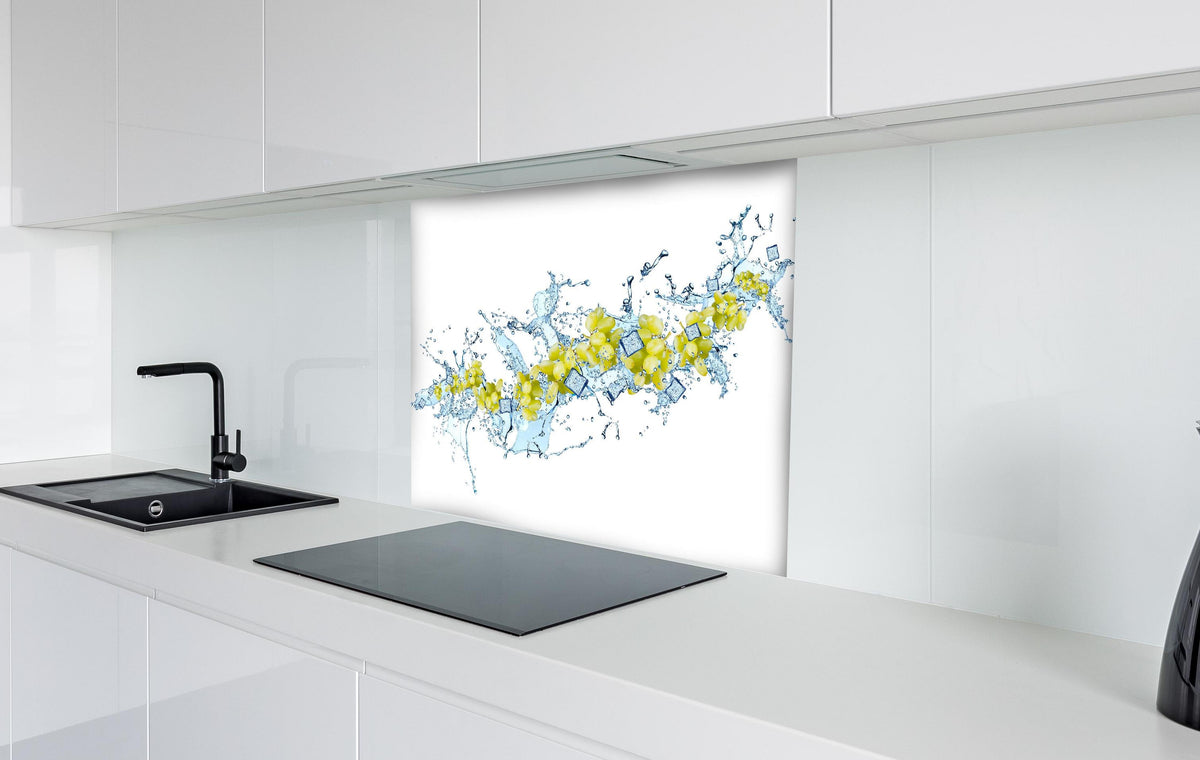 Spritzschutz - Gelbe Trauben mit dynamischem Wasser Splash hinter einem Cerankochfeld zwischen Holz-Kochutensilien