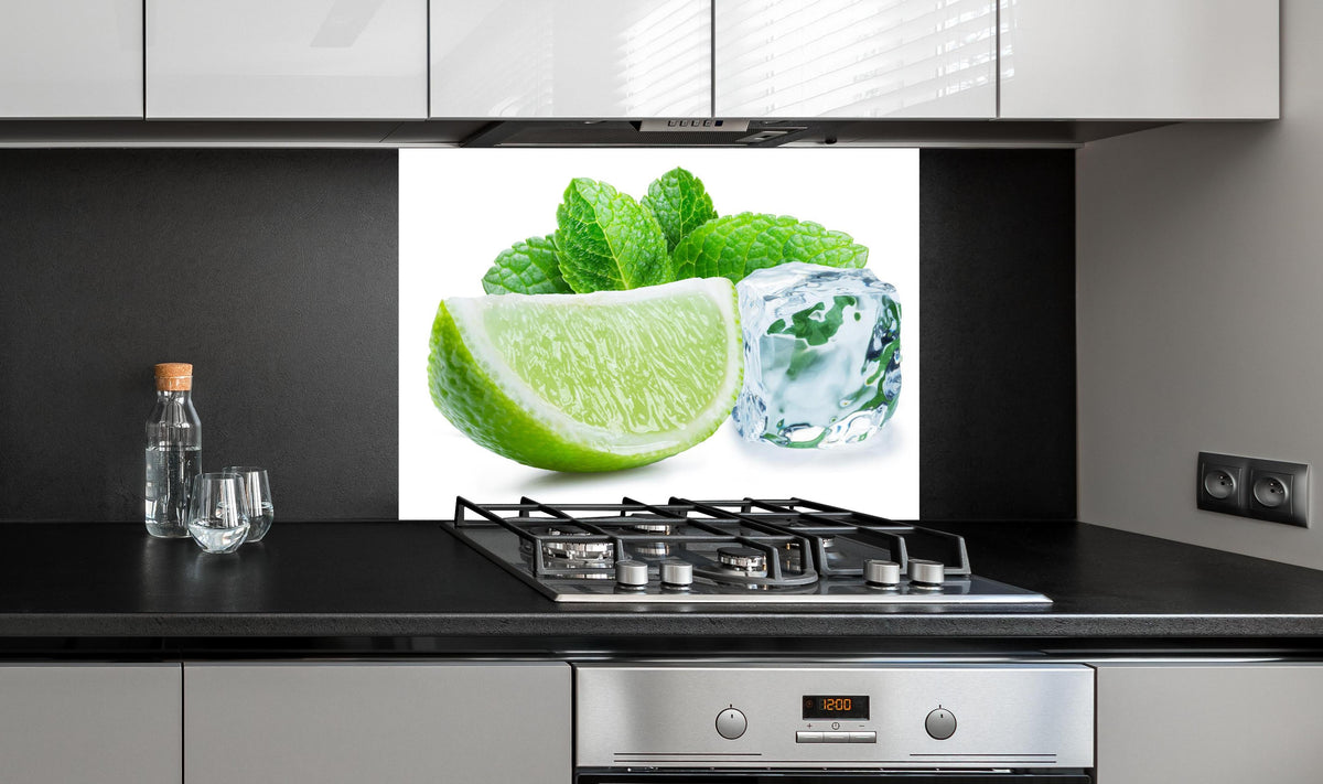 Spritzschutz - Limettenscheibe mit Eis und Minze hinter einem Cerankochfeld zwischen Holz-Kochutensilien