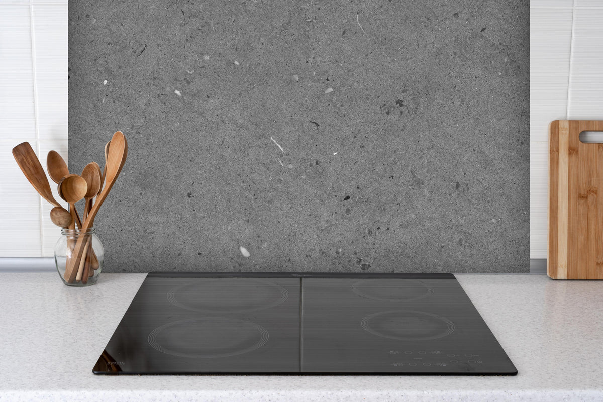 Spritzschutz - Grauer Marmor im Asphaltdesign hinter einem Cerankochfeld zwischen Holz-Kochutensilien
