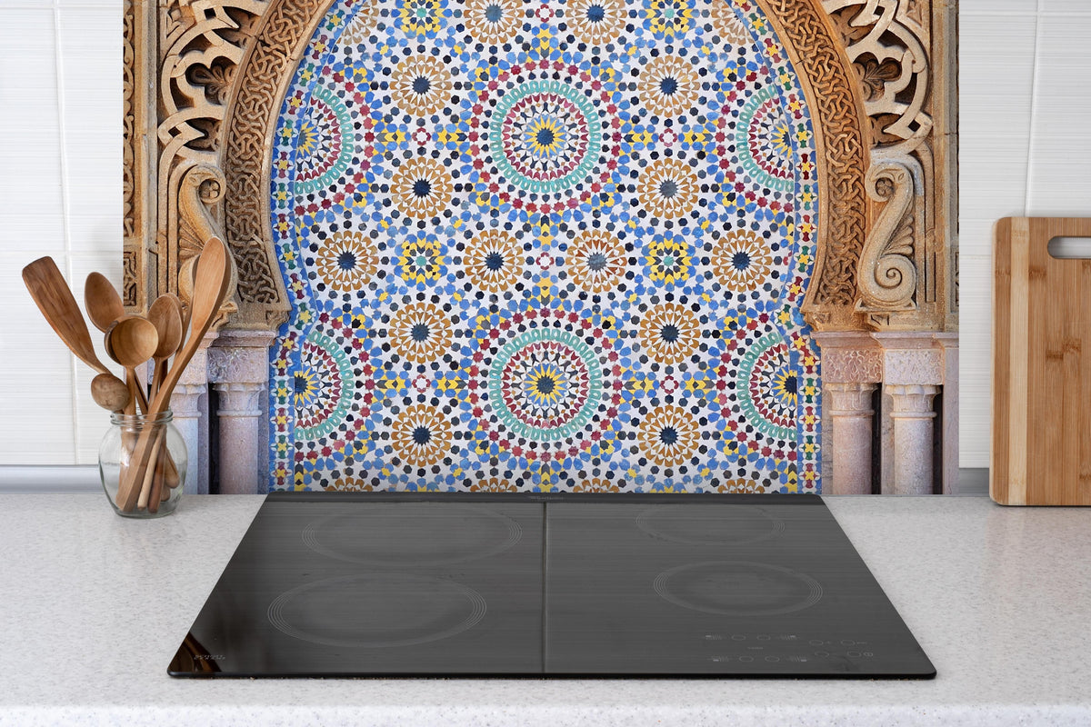 Spritzschutz - Verzierter Brunnen mit Mosaikfliesen in Rabat hinter einem Cerankochfeld zwischen Holz-Kochutensilien
