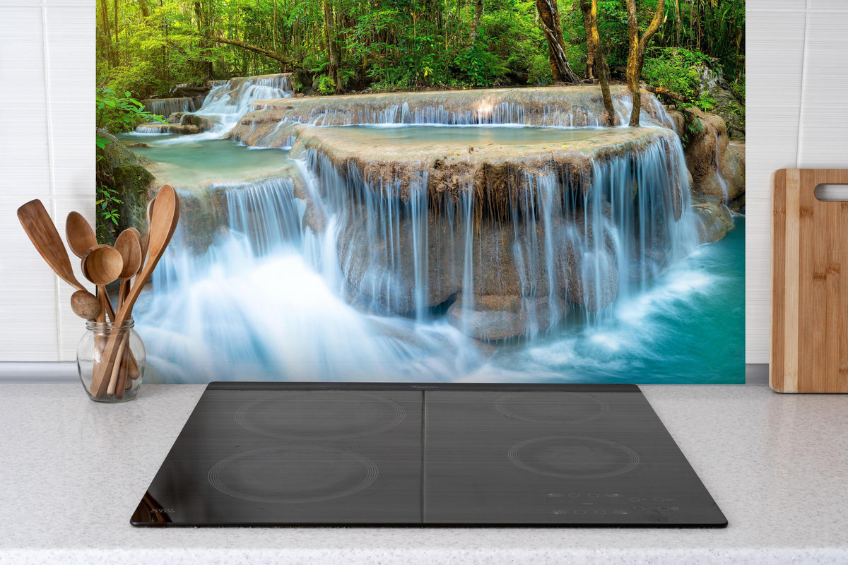 Spritzschutz - Wasserfall im Wald von Thailand hinter einem Cerankochfeld zwischen Holz-Kochutensilien
