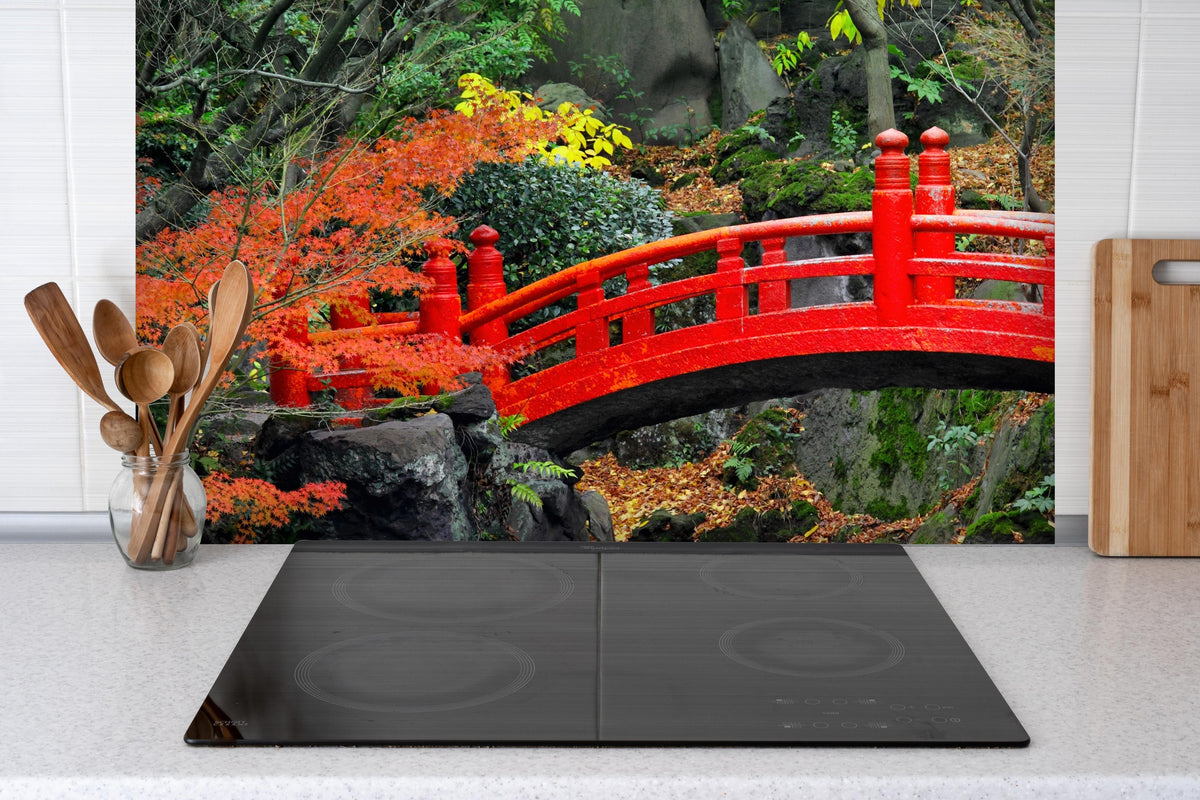 Spritzschutz - traditioneller japanischer Garten an Teich  hinter einem Cerankochfeld zwischen Holz-Kochutensilien
